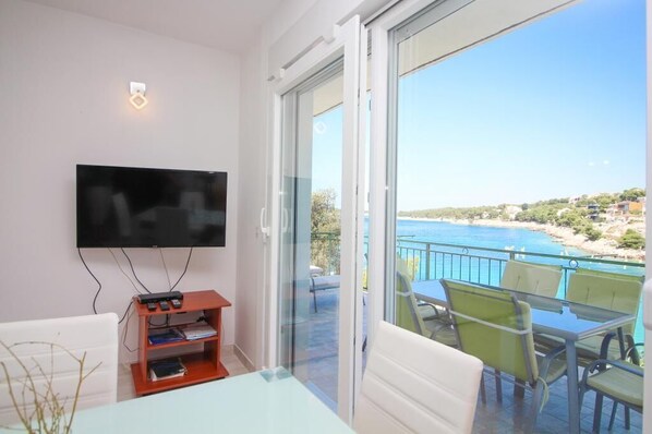 Un balcón con televisor, mesa y sillas, con vista a una playa y al mar.