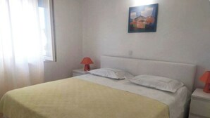 A neatly made bed with a yellow bedspread, a white headboard, and a red lamp on a bedside table. - Apartments Roko (Primosten)