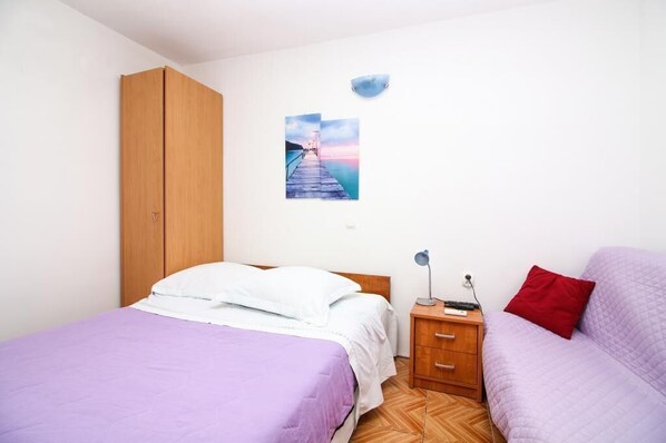 Une chambre avec deux lits, une armoire en bois, une table de chevet avec une lampe et un luminaire fixé au mur.