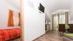 A compact living space with a bed, kitchenette, dining area, and a TV mounted on the wall. - Apartment Tamara (Okrug)