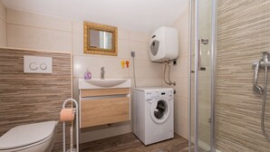 A compact bathroom with a toilet, sink, washing machine, and shower. - Apartment Tamara (Okrug)