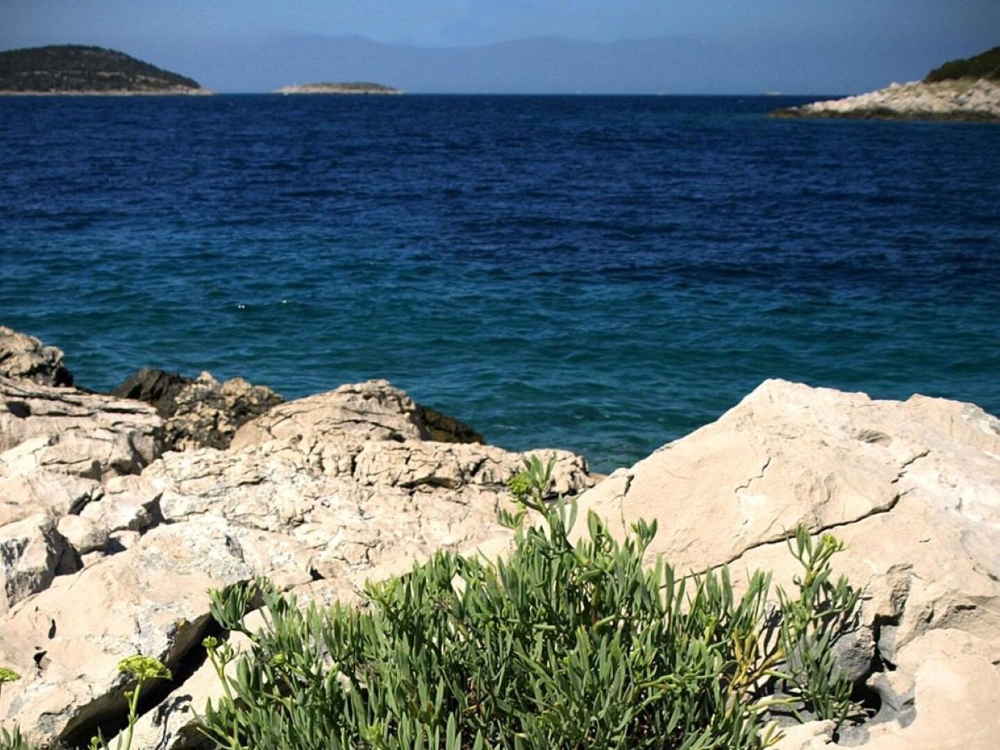 Una costa rocosa con mar azul cristalino y islas a lo lejos.