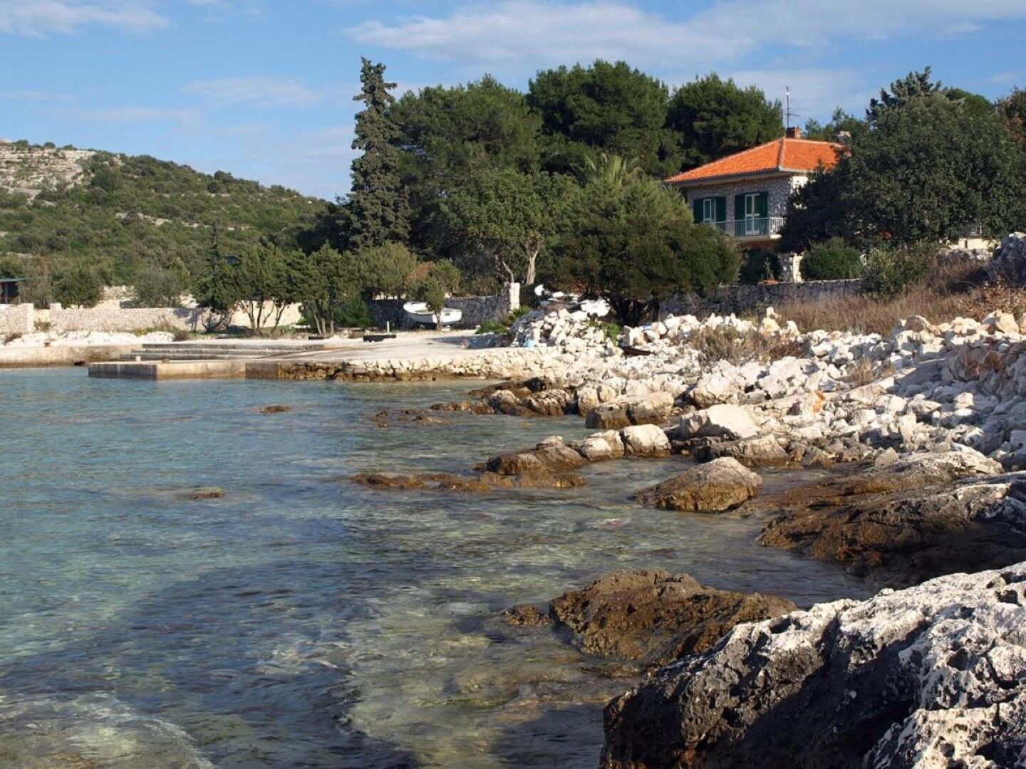 A coastal area with clear water, rocky shore, and a house with a red roof.