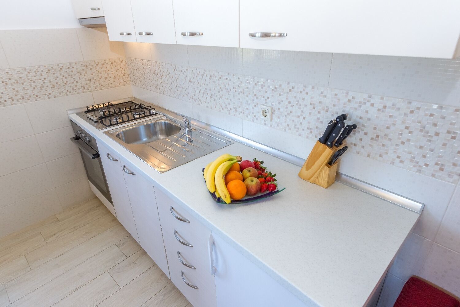A modern kitchen with white cabinets, a stainless steel sink, a gas stove, and a fruit bowl on the counter.