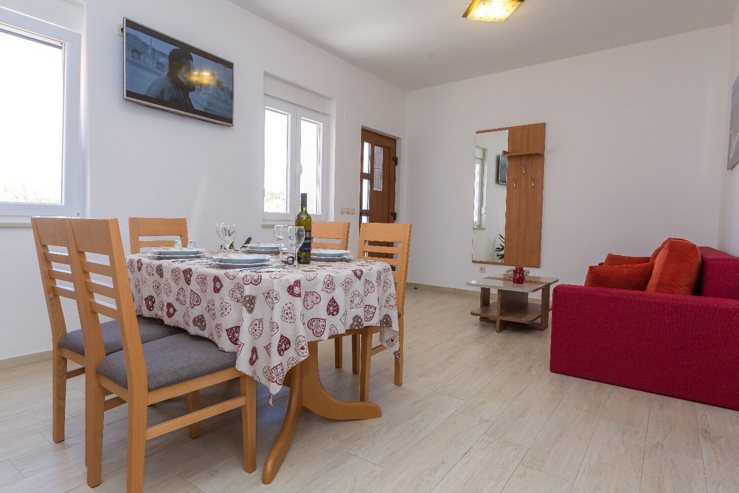 Un comedor con una mesa dispuesta para cuatro personas, sillas de madera y un sofá rojo en la sala.