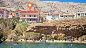 A coastal area with buildings, a rocky cliff, and a beach with people. - Apartments Star 3 (Pag)
