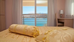 A hotel room with a bed, a desk, and a view of a body of water and mountains. - Apartments Star 3 (Pag)
