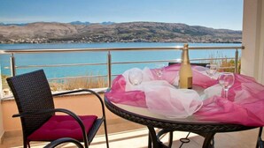 A balcony with a table set for two, overlooking a body of water and hills. - Apartments Star 3 (Pag)