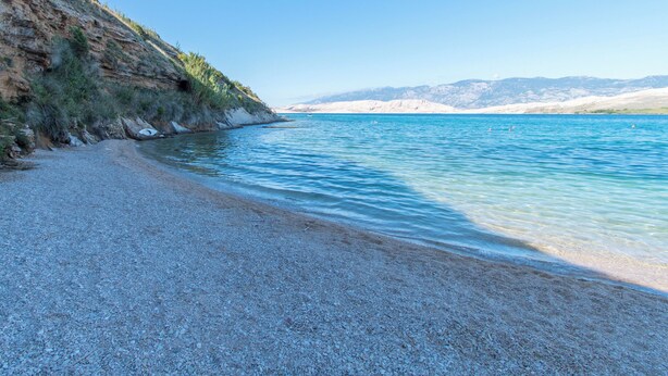 A pebble beach with clear blue water and a rocky cliff. - Apartments Star 3 (Pag)
