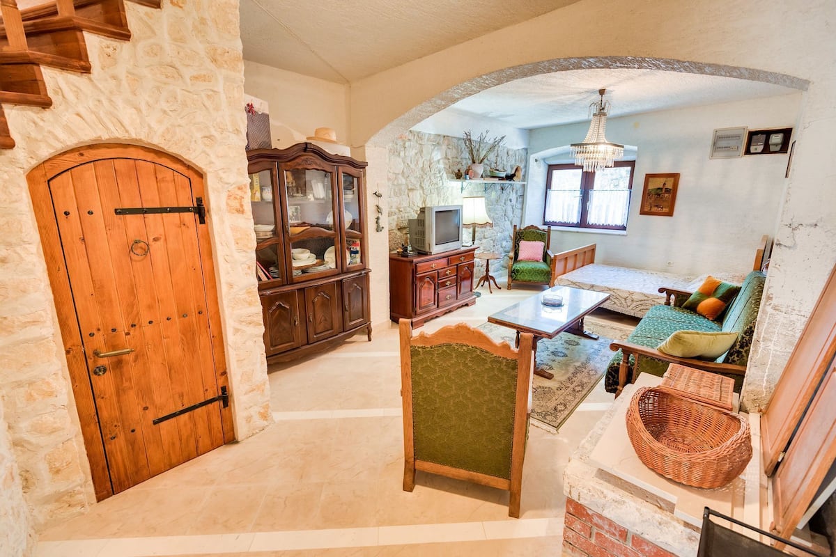 A cozy living room with a stone wall, wooden furniture, a television, and a fireplace.