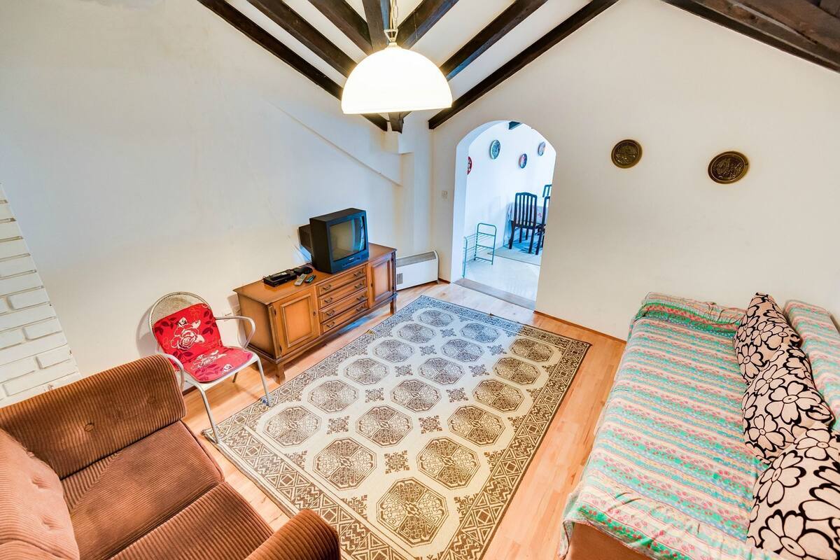 A cozy room with a sofa, a TV, a patterned rug, and a bed with a floral bedspread.
