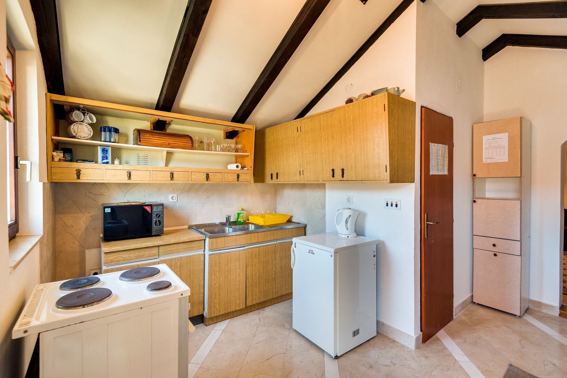 A compact kitchen with wooden cabinets, a microwave, a small refrigerator, and a stove.
