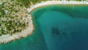 An aerial view of a beach with clear turquoise waters, a sandy shore, and a line of beach umbrellas. - Apartments Ani (Crikvenica)