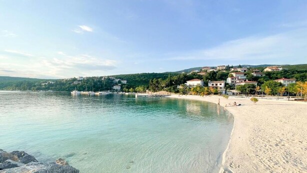 A coastal beach with clear water, a sandy shore, and buildings in the background. - Apartments Ani (Crikvenica)
