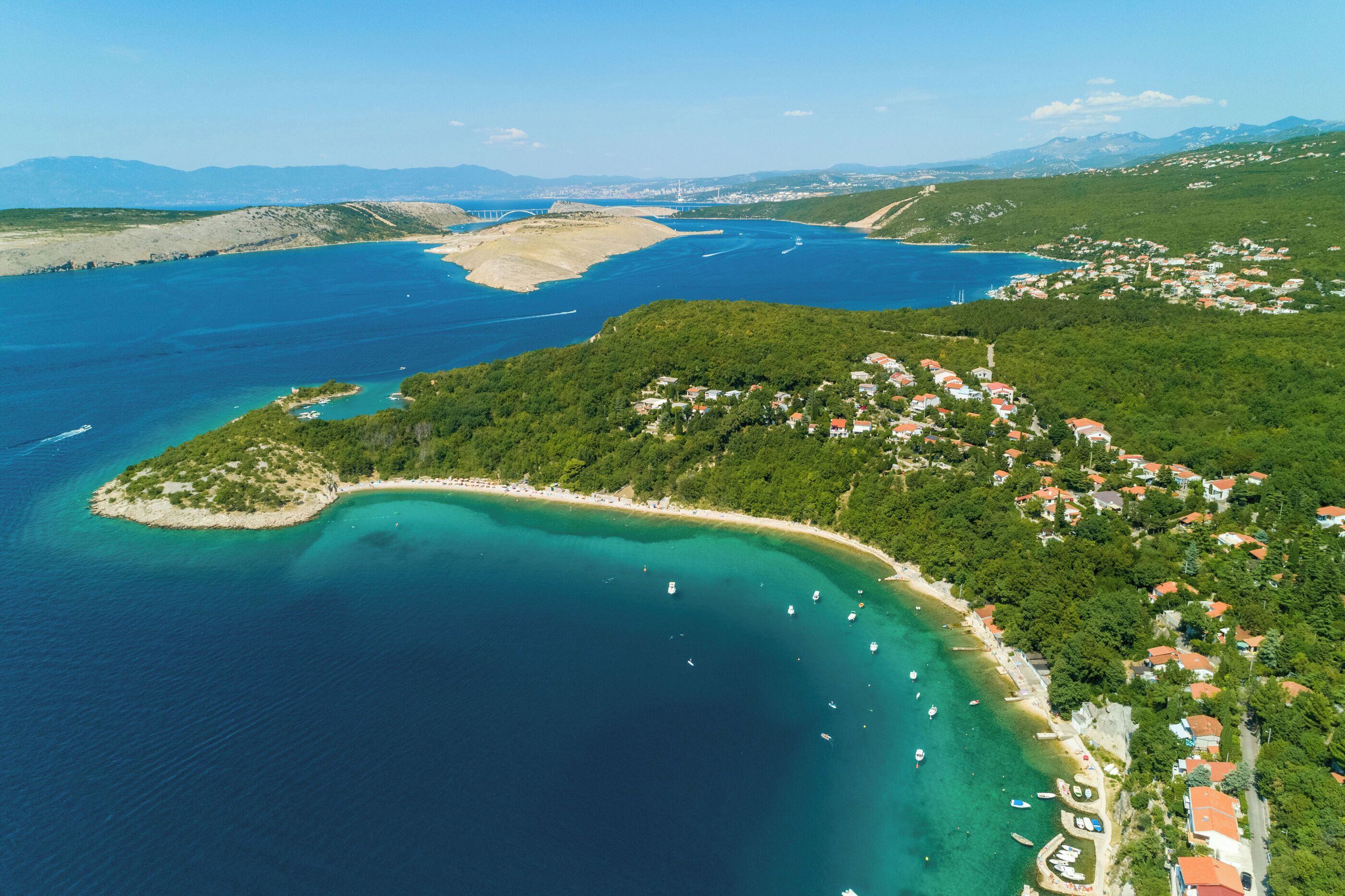 An aerial view of a coastal area with a beach, boats, and a village.