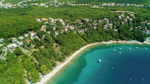 An aerial view of a coastal area with a beach, clear turquoise waters, and a densely populated residential area with red-roofed houses. - Apartments Ani (Crikvenica)