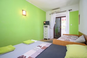 A room with two beds, a television on a cabinet, and a window with curtains. - Apartments Ani (Crikvenica)