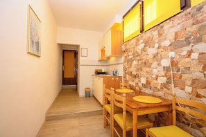A narrow hallway leading to a kitchen with a stone wall, wooden cabinets, and a dining table with chairs. - Apartments Ani (Crikvenica)