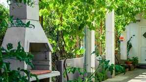 Un espacio al aire libre con mobiliario de hormigón, que incluye una parrilla empotrada, rodeado de abundante vegetación y plantas en macetas.