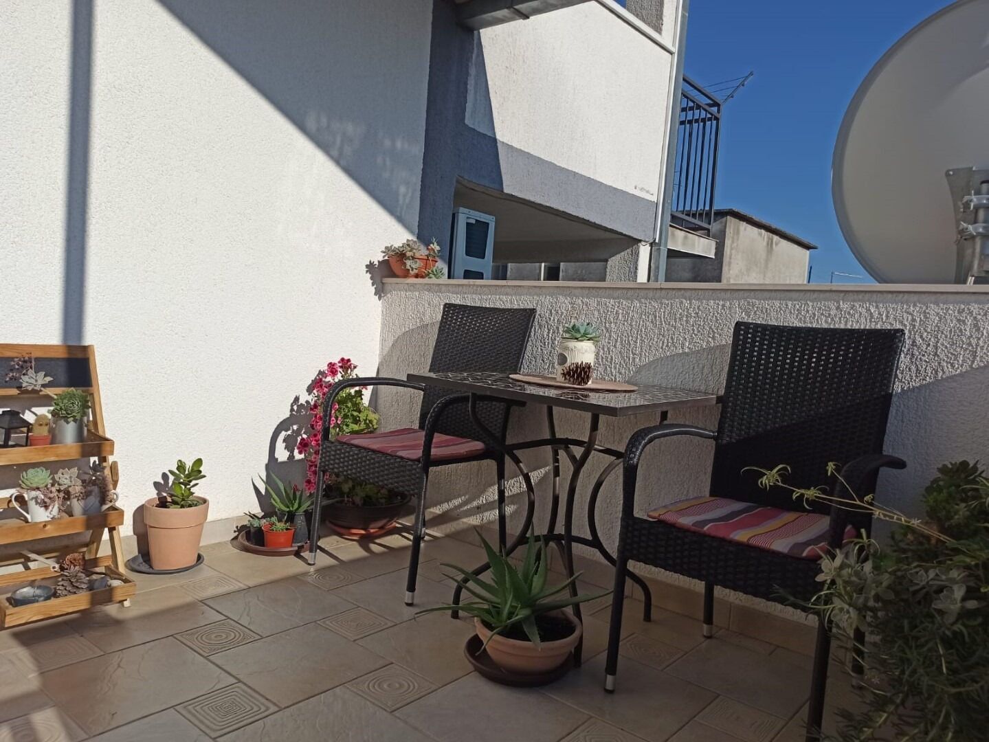 A balcony with two wicker chairs, a small table, and various potted plants.
