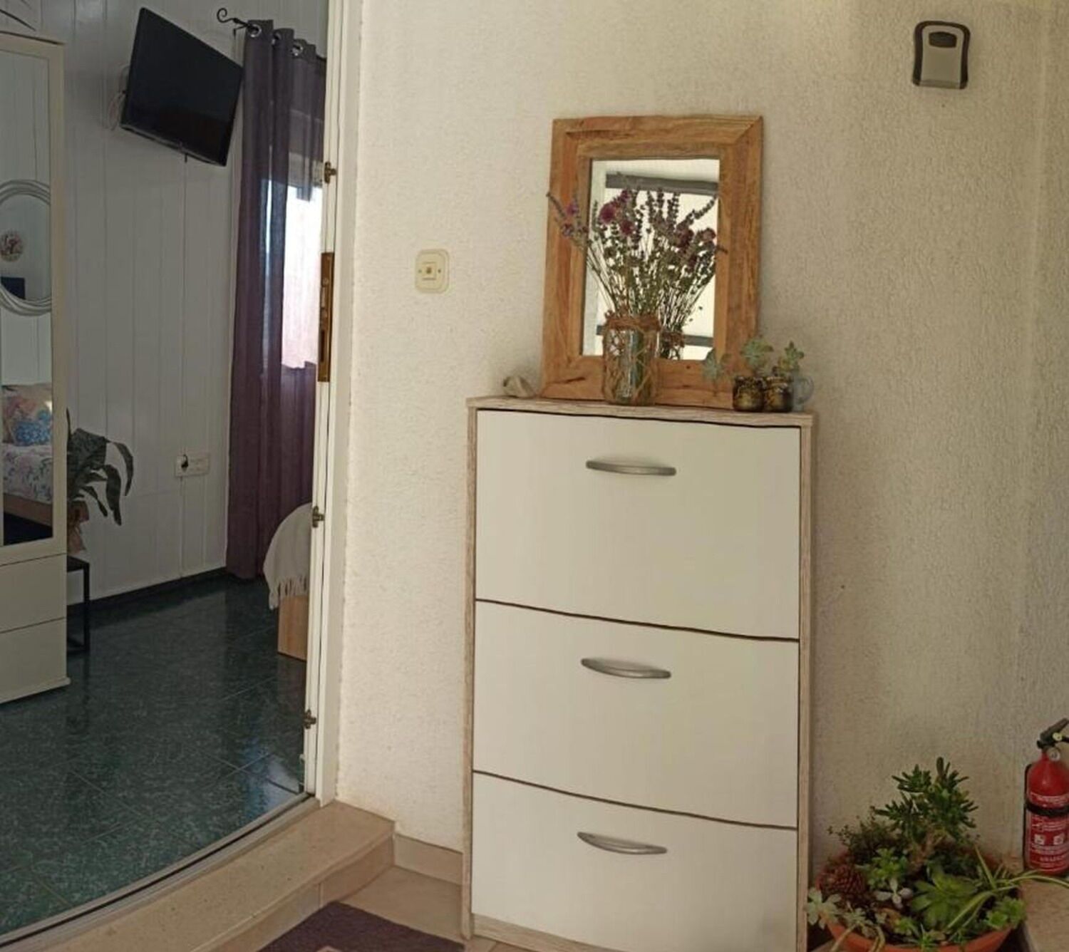 Ein Zimmer mit einem weißen Schminktisch, einem Spiegel und einer kleinen Pflanze darauf.
