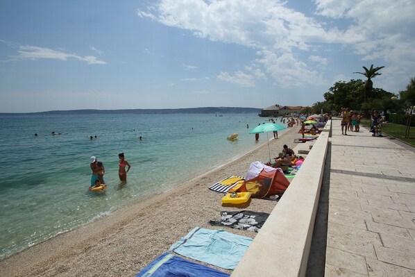 A beach with clear water, umbrellas, and people swimming. - Apartment Jurica (Kastela)