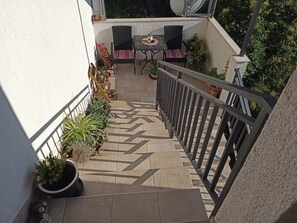 A sunlit outdoor area with a tiled floor, a small table with chairs, and potted plants. - Apartment Jurica (Kastela)