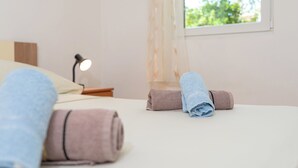 A neatly made bed with rolled towels, a bedside lamp, and a window with a view of greenery.