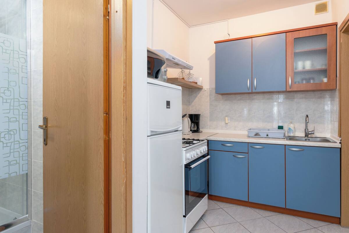 A compact kitchen with a white refrigerator, stove, and oven, blue cabinets, and a wooden door.