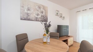 A modern living room with a round wooden table, two chairs, a TV, and a painting on the wall.