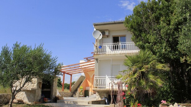 A two-story building with a balcony, a satellite dish, and a stone wall entrance.