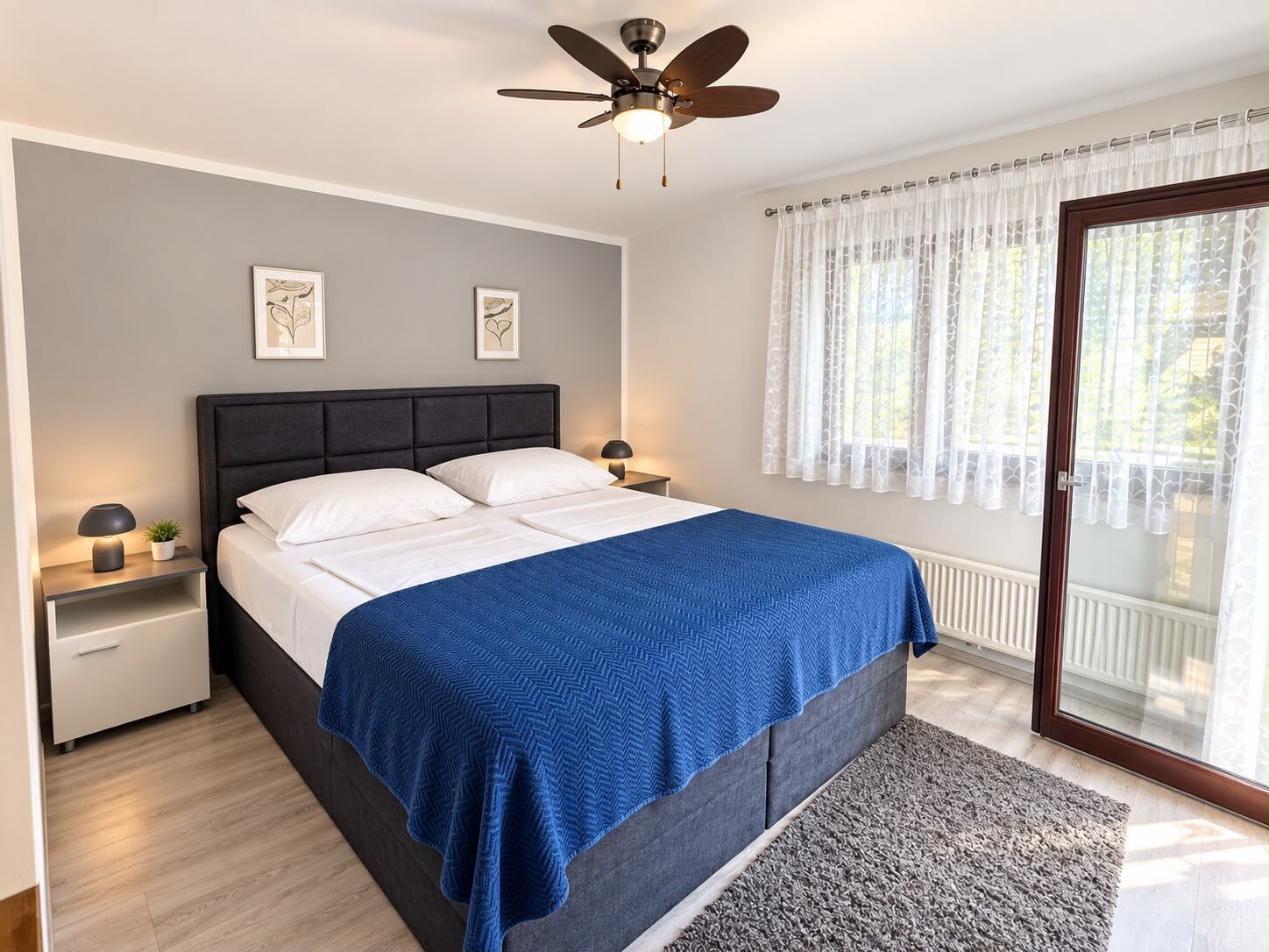 Een slaapkamer met een bed, nachtkastjes, een plafondventilator en een raam met gordijnen.