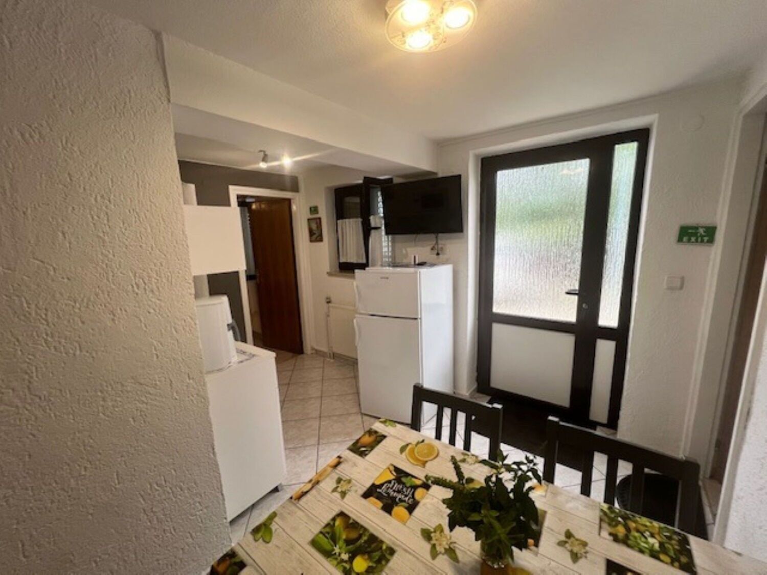 Een compacte keuken met witte apparaten, een eethoek met een tafel voor twee personen, en een uitzicht op de aangrenzende woonkamer.