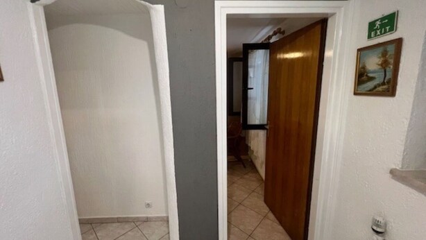 Un couloir avec une porte blanche donnant sur une pièce, un panneau de signalisation verte indiquant la sortie, et un tableau encadré accroché au mur.