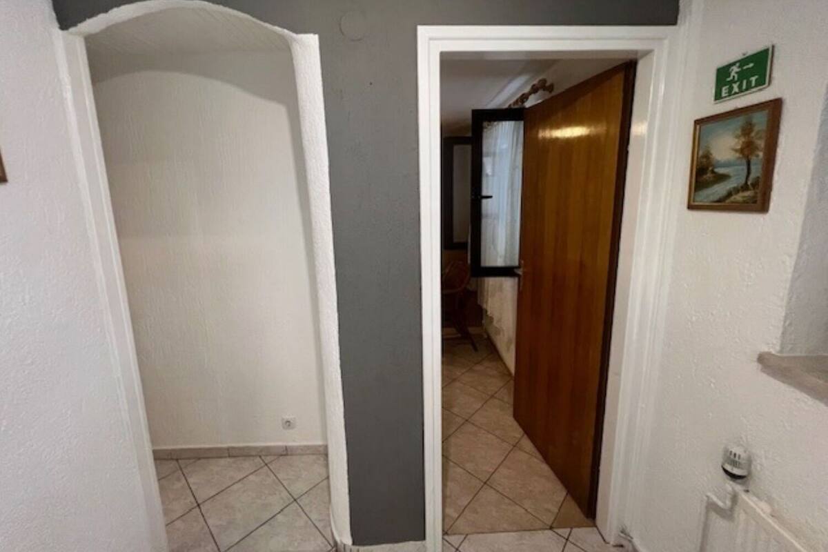 A hallway with a white door leading to a room, a green exit sign, and a framed picture on the wall.