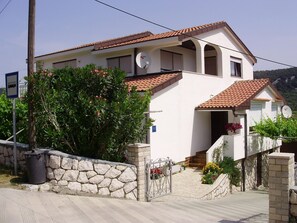 A two-story house with a stone wall entrance, a satellite dish, and a small garden with flowers. - Apartment Ani (Rab)