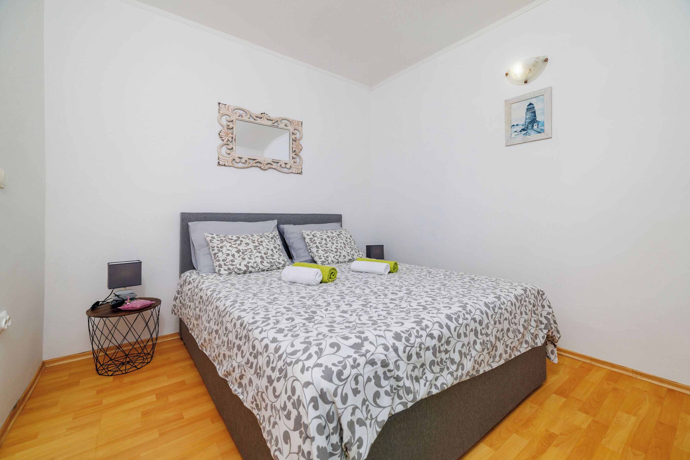 A bedroom with a bed, a bedside table, a lamp, a picture frame, and a wall-mounted light fixture.