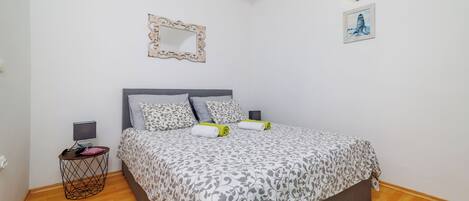 A bedroom with a bed, a bedside table, a lamp, a picture frame, and a wall-mounted light fixture.