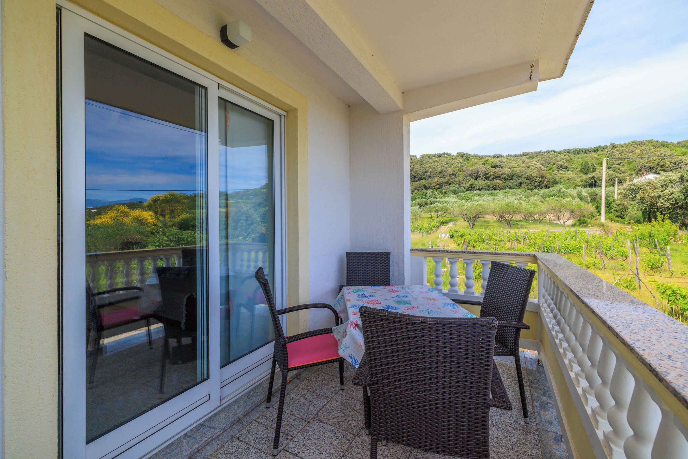 A balcony with a table and chairs, a glass door, and a view of a green landscape.