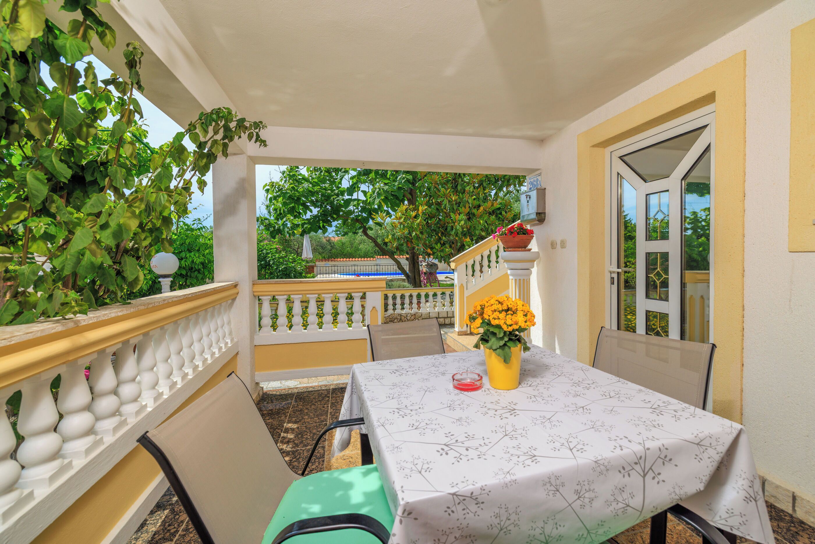 A balcony with a table set for two, chairs, and a potted plant with yellow flowers.