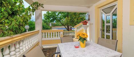 A balcony with a table set for two, chairs, and a potted plant with yellow flowers.