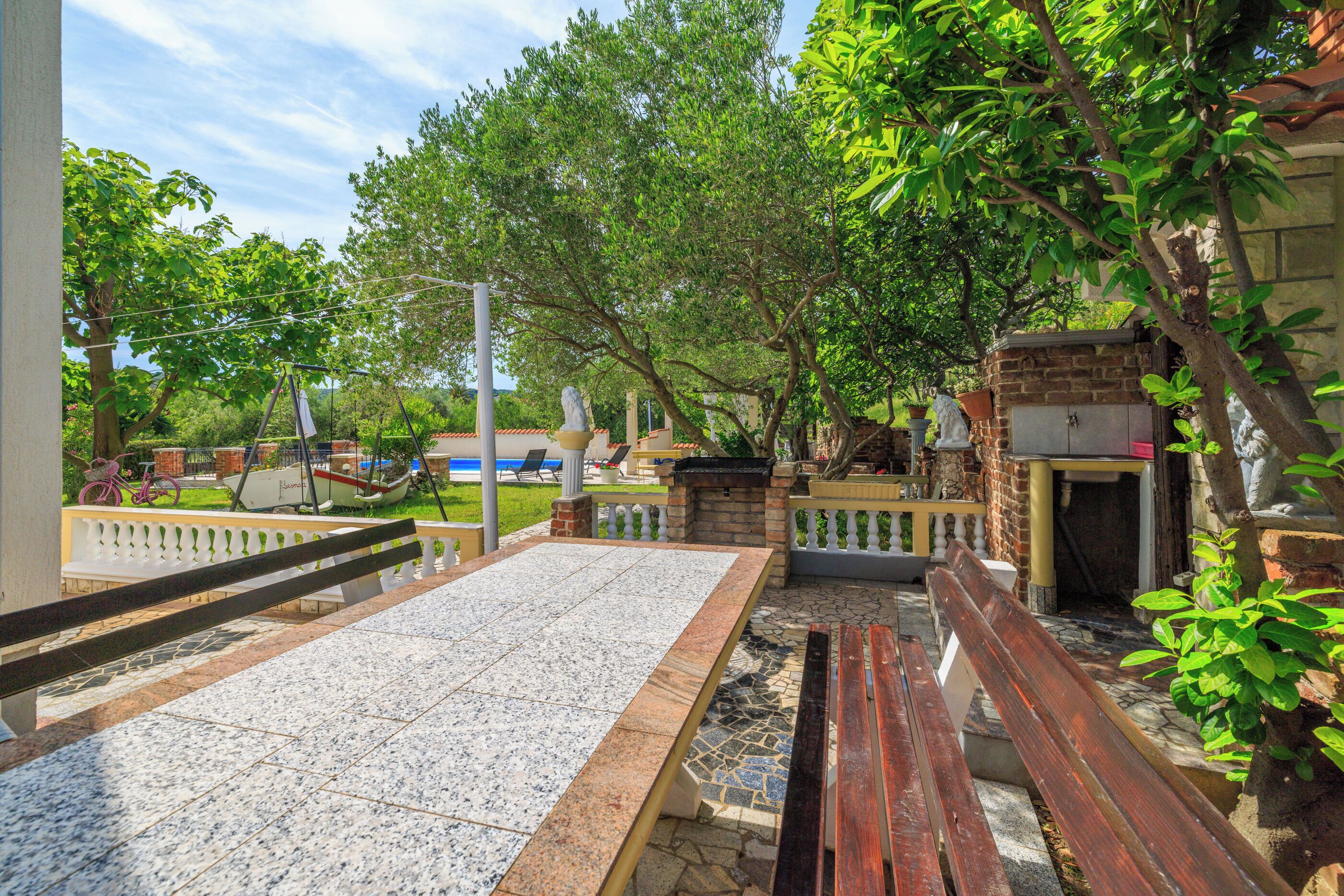 An outdoor patio area with a tiled table, wooden benches, and a brick barbecue station.