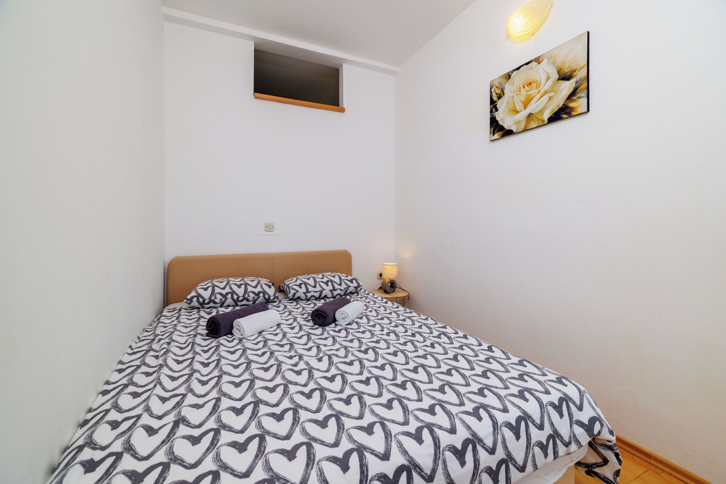A bedroom with a bed, a nightstand, a wall-mounted shelf, and a framed picture.