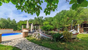A stone pathway leading to a swimming pool, surrounded by lush greenery and a gazebo. - Apartments Roby (Rab)