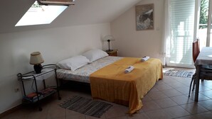 Een slaapkamer met een bed, nachtkastje, lamp, stoel, raam en een schilderij aan de muur.