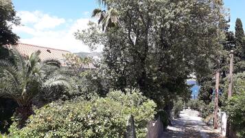 Uma passagem bordeada por vegetação exuberante e plantas floridas, conduzindo a um edifício com telhado de telhas vermelhas.