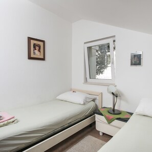 Habitación individual con ventana, mesita de noche con lámpara y dos cuadros en la pared.