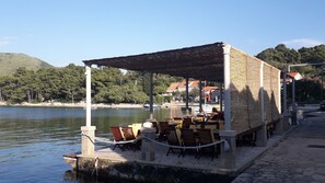 Un restaurante frente al agua con terraza, un muelle de piedra y vistas al lago y las colinas.
