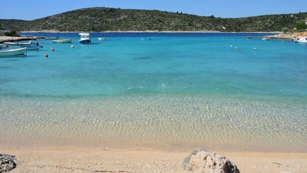 A beach with clear turquoise water, boats, and a hilly landscape in the background. - Apartments Branka (Rogoznica)