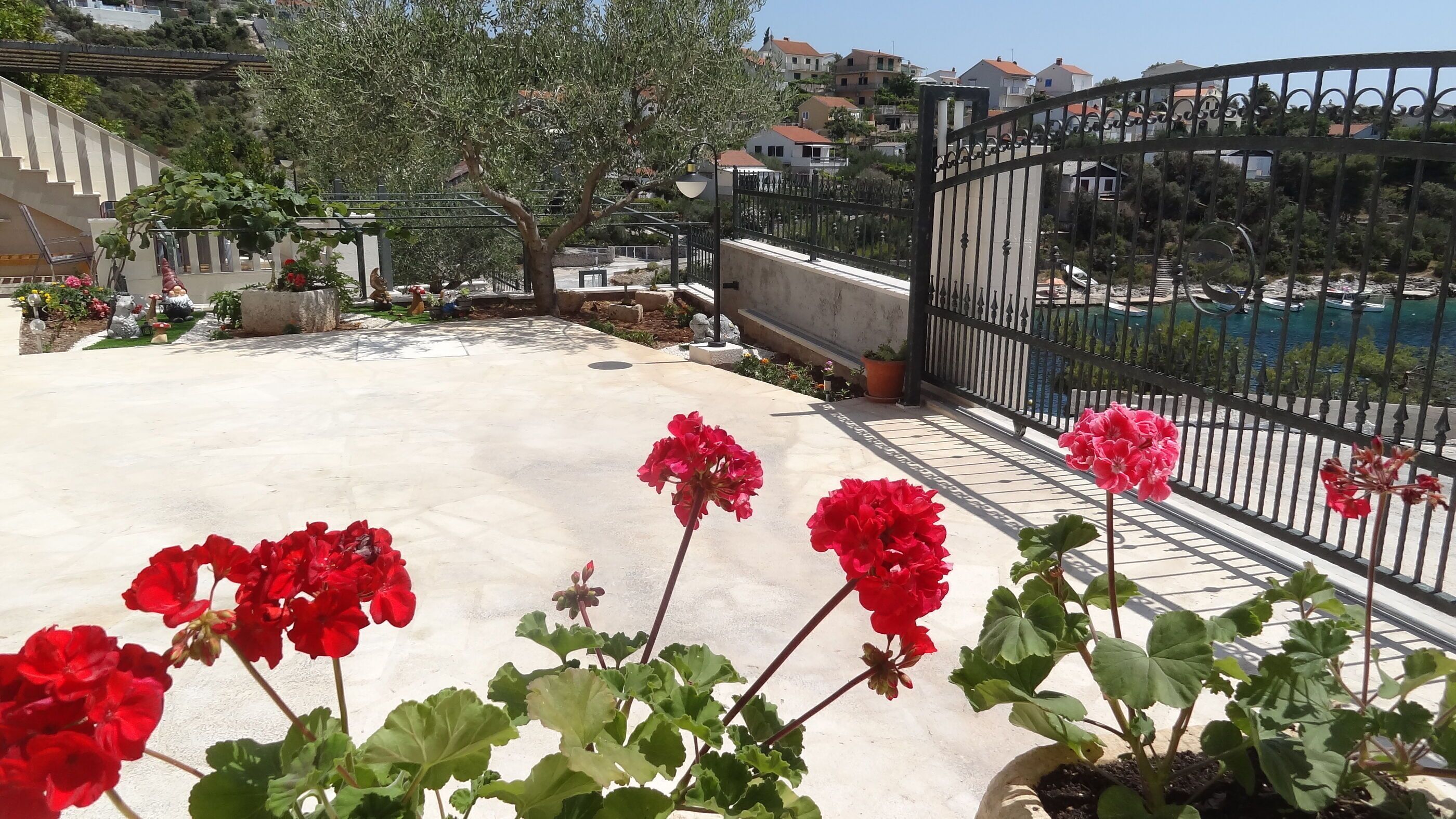 Une terrasse sur le toit agrémentée de géraniums rouges, une porte en métal et une vue sur un quartier résidentiel et un plan d’eau.